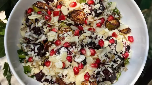 Foto de un plato de ensalada con coles de bruselas asadas, granada roja, arroz, alubias.