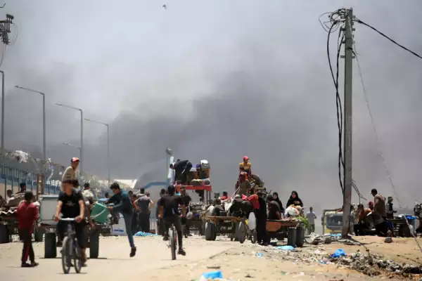 Los palestinos huyen con sus pertenencias mientras el humo se eleva en el fondo, en el área de Tel al-Sultan en Rafah, en el sur de la Franja de Gaza, el 30 de mayo de 2024, en medio del conflicto en curso entre Israel y el grupo militante Hamas