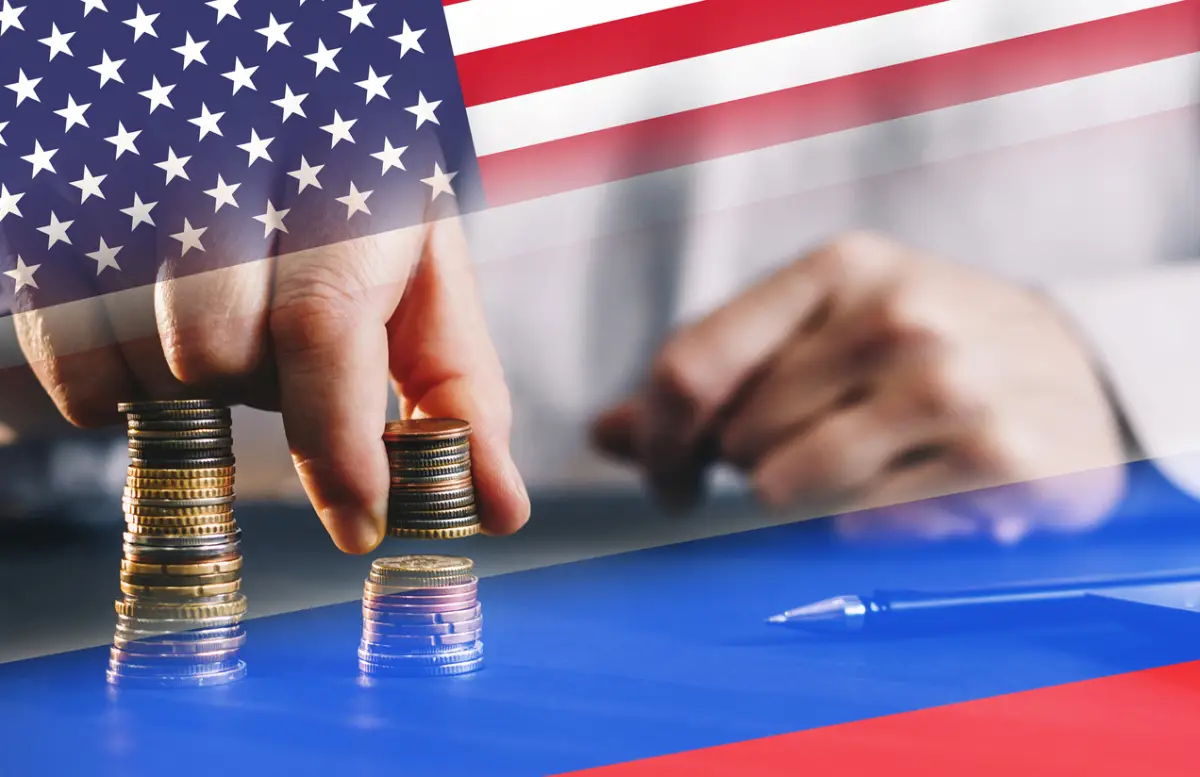 Una persona apila monedas con las banderas de Estados Unidos y Rusia de fondo. 