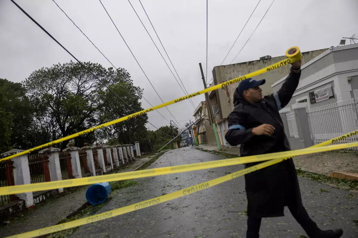 Un oficial de policía acordona una calle donde un poste de línea eléctrica se apoya en una casa después de la tormenta tropical Ernesto en Fajardo, Puerto Rico, el 14 de agosto de 2024.