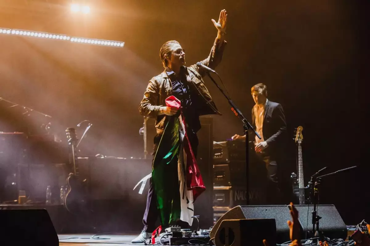 Foto de integrantes de Interpol en un escenario sosteniendo una bandera mexicana.