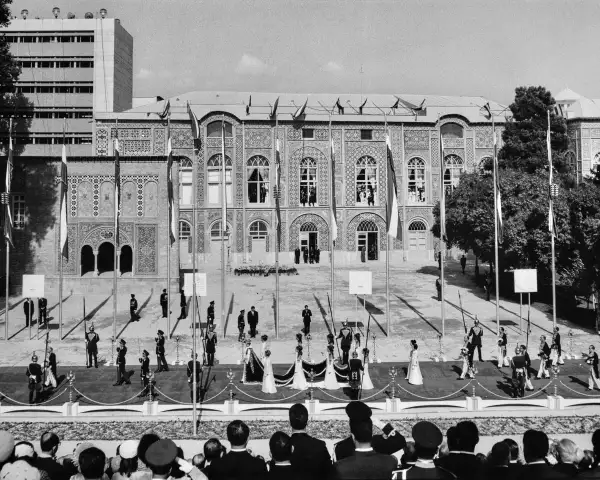 Vista general de la emperatriz Farah Pahlavi y los asistentes caminando en una procesión en el patio del Palacio Golestán después de su ceremonia de coronación en Teherán, Irán, el 26 de octubre de 1967. En primer plano, se muestra a los visitantes viendo la procesión.