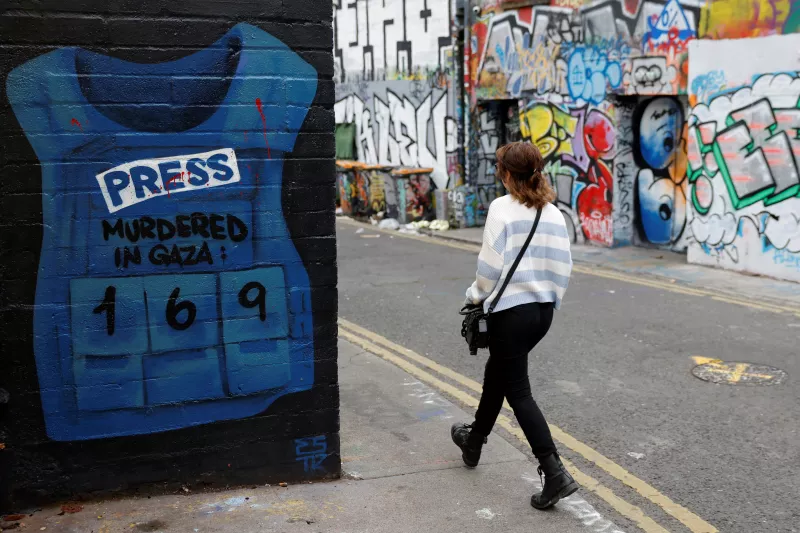 Una mujer pasa junto a un mural en apoyo de los palestinos con una camisa de prensa con varios periodistas asesinados en Gaza, en medio del conflicto en curso Israel-Hamas, en Dublín, Irlanda, el 22 de septiembre de 2024.