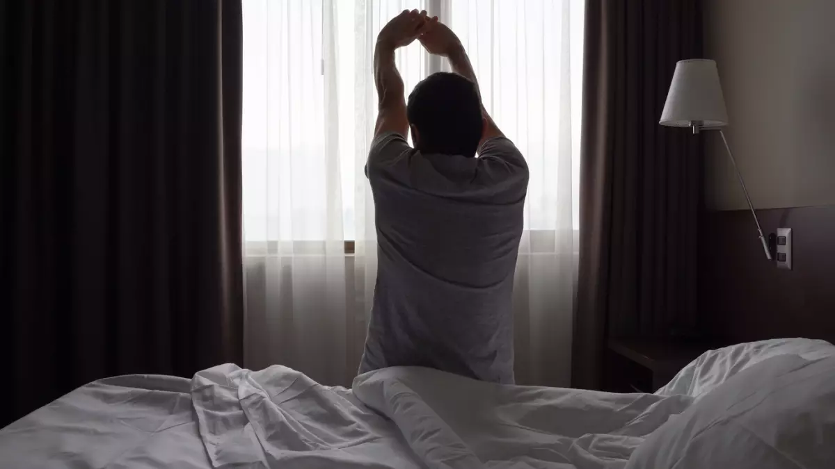 Silhouette of man sitting on bed stretching up arms