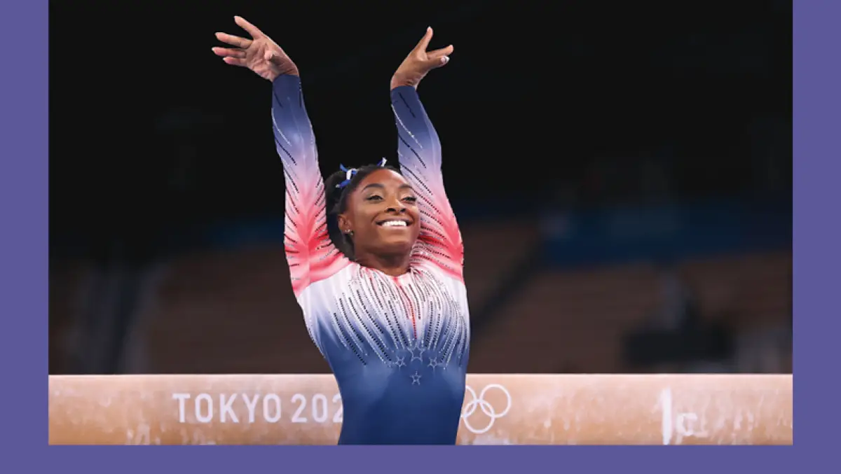 Foto de Simone Biles con el uniforme de estados unidos levantando sus brazos y sonriendo durante su presentación en Tokio 2020.