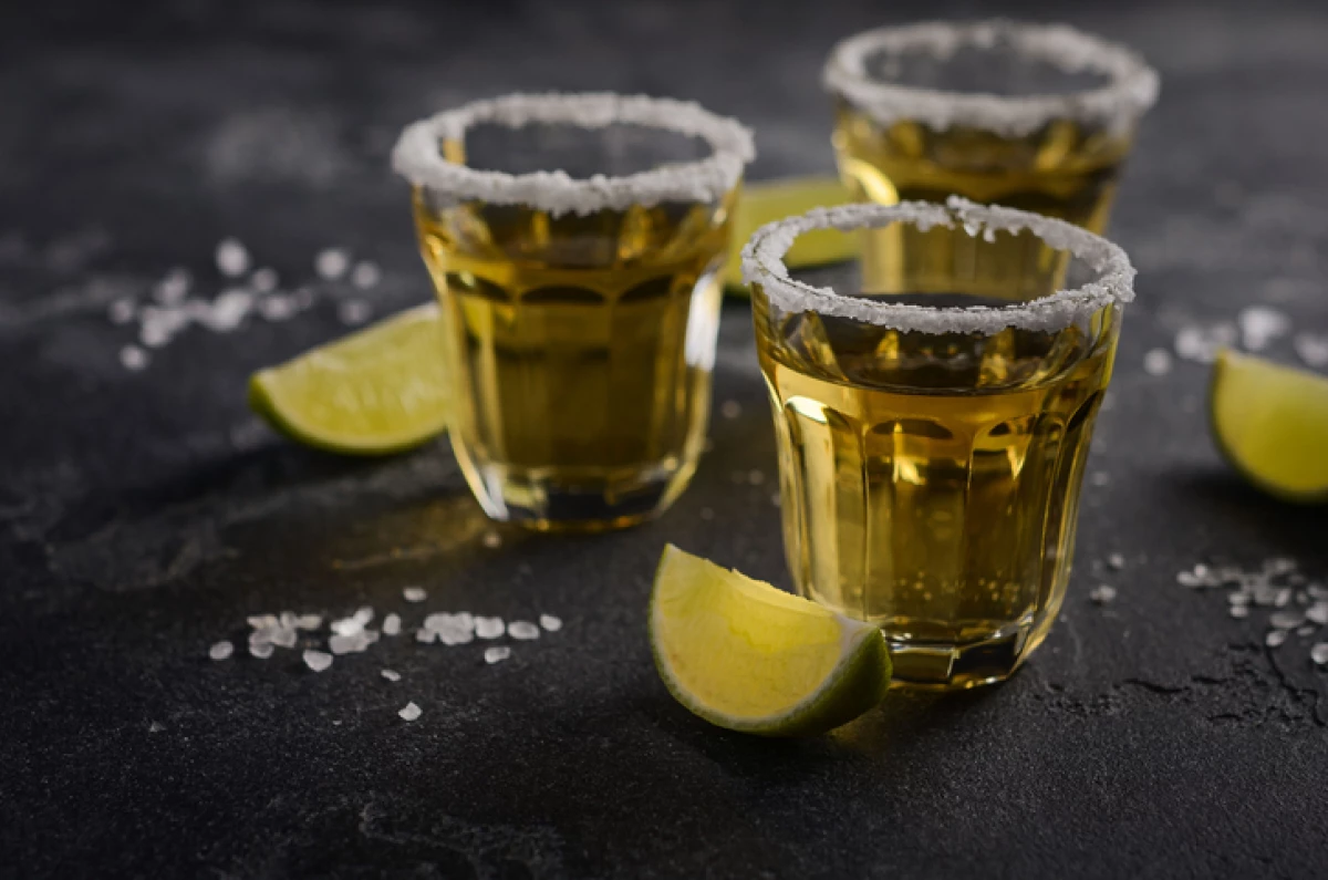 Gold tequila with lime and salt rim on dark stone or concrete background.