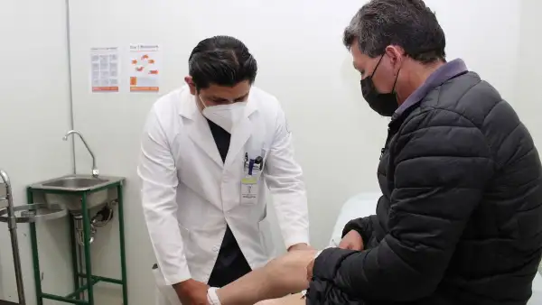 Un médico que viste bata blanca revisa la pierna de un paciente. 