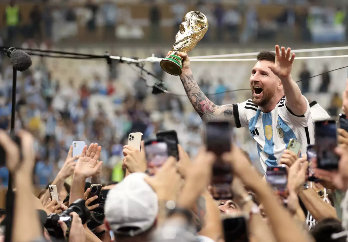 Foto de Lionel Messi cargando la copa del mundo en la mano izquierda mientras es cargado en hombros por sus compañeros al ganar el Mundial de Qatar 2022.
