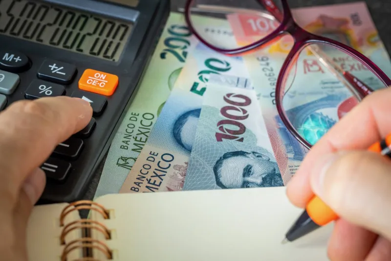 Un empresario hace la estimación del pago de sus impuestos con calculadora, pluma y libreta en mano. 
