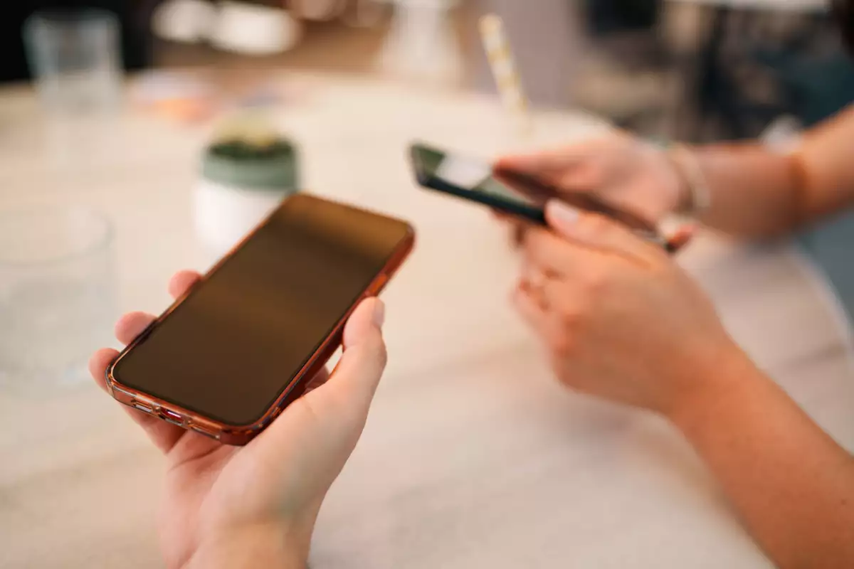 Una vista en primer plano de dos teléfonos que se mantienen juntos, lo que sugiere el intercambio de datos o la colaboración entre dos amigos. La imagen captura la intimidad y la interacción digital en un entorno informal al aire libre.