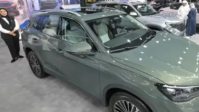 Una mujer vestida de negro y blanco junto a un auto color gris nuevo de la marca volkswagen.jpg