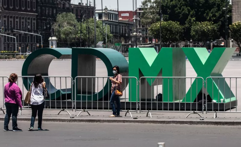 Turistas se toman una fotografía en las emblemáticas letras "CDMX" ubicadas en la Plancha del Zócalo Capitalino, la cual se encuentra cercada con vallas metálicas para evitar aglomeraciones