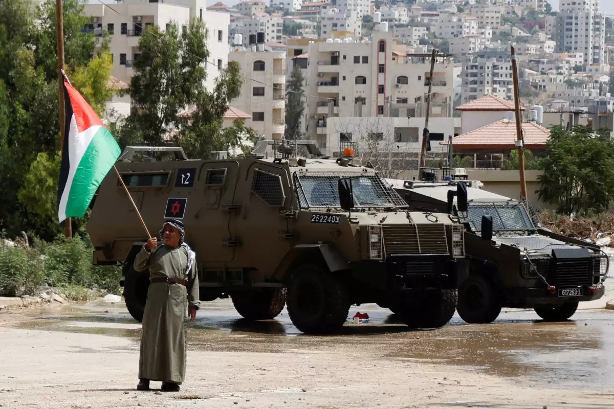 Un hombre sostiene la bandera palestina junto a vehículos militares israelíes durante la redada en Tulkarm, en Cisjordania ocupada por Israel, el 22 de agosto de 2024.