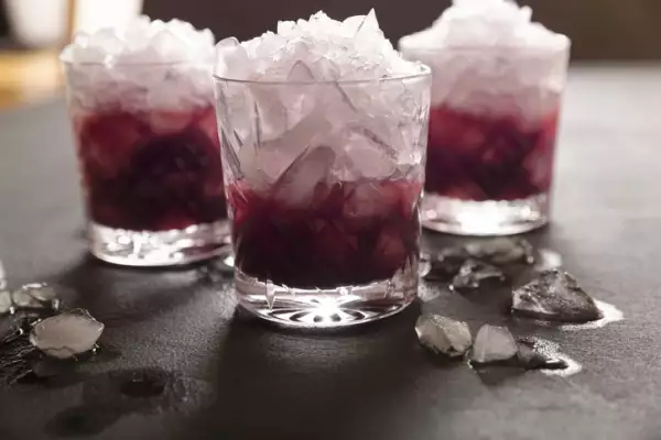 Vasos de vidrio con muchos hielos y bebida de color rojo sobre una mesa oscura.