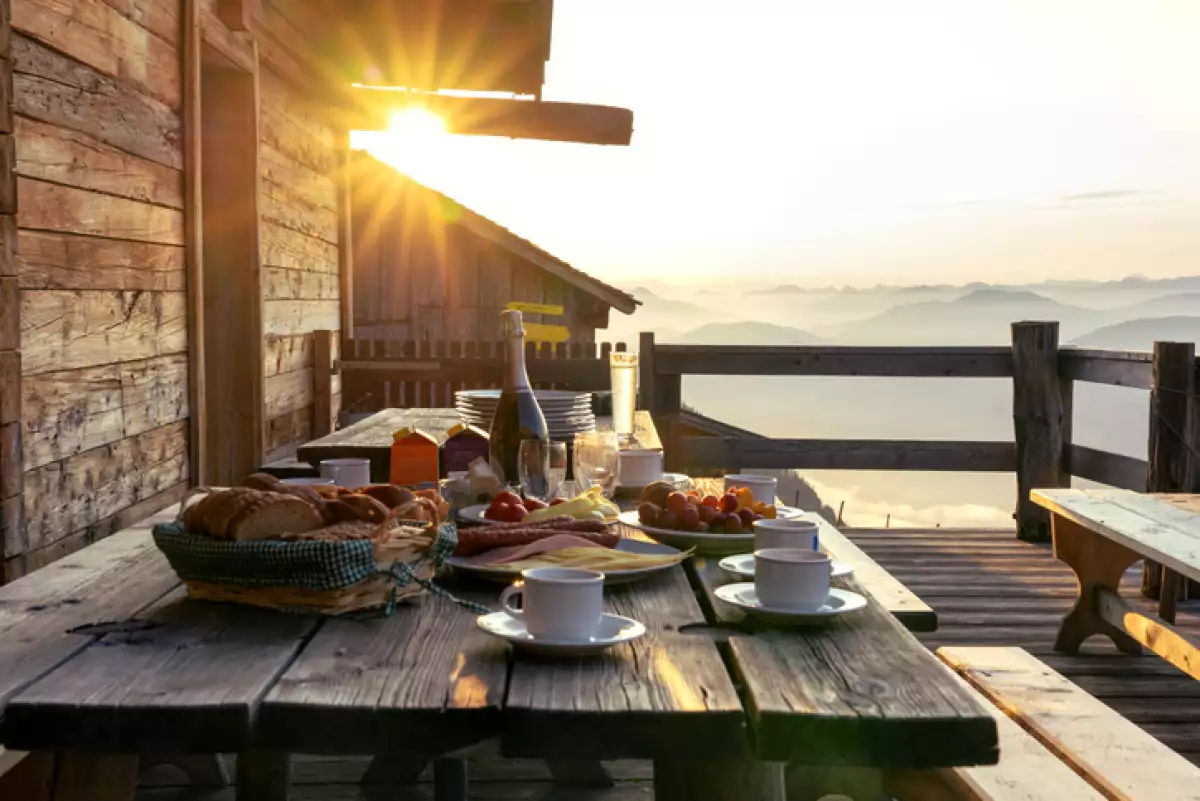 Mesa de desayuno en el patio de terraza de madera rústica de una cabaña hutte en Tirol alm al amanecer.