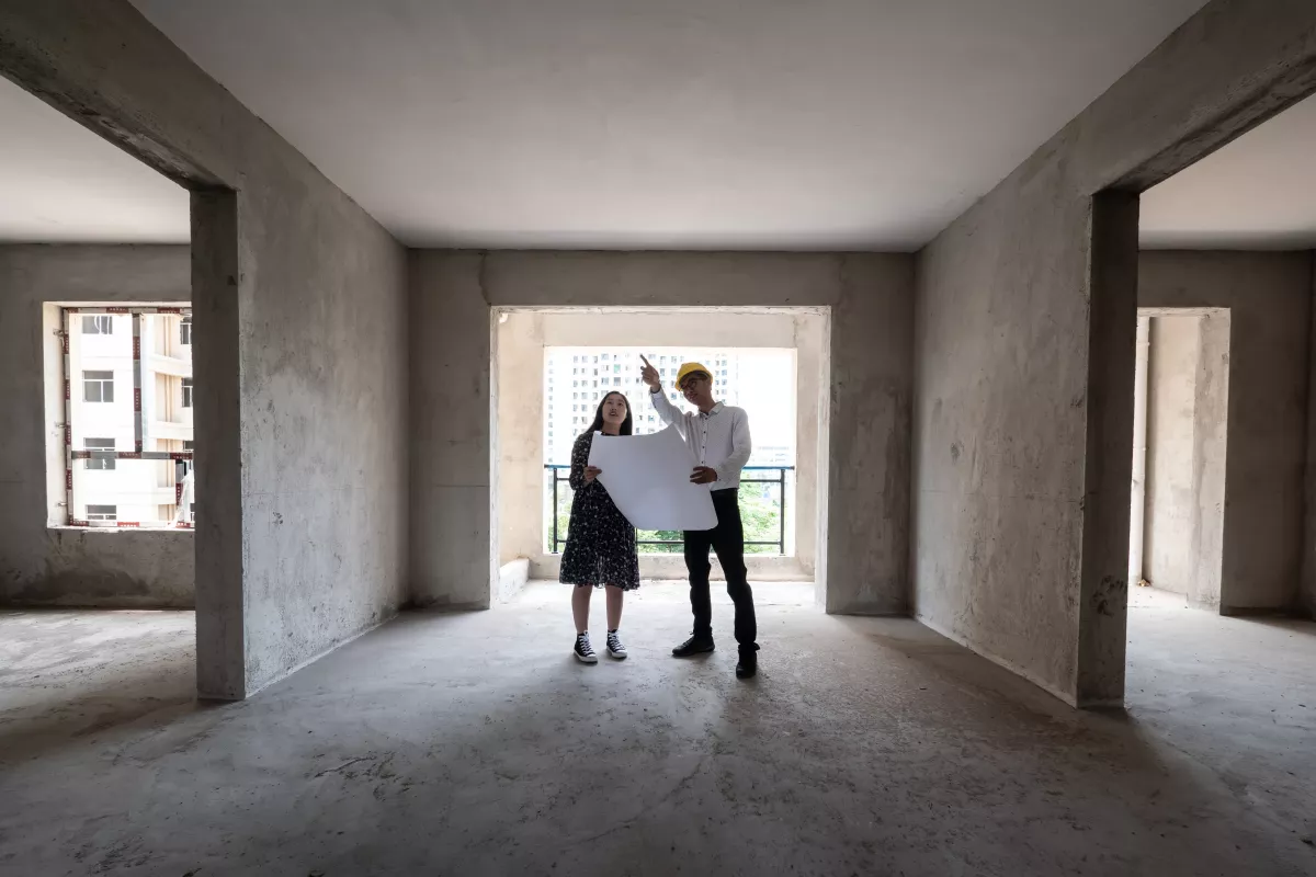 Dos personas viendo planos en una vivienda en obra gris