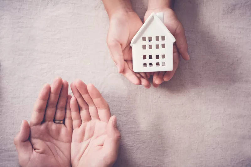 Adult and child hands holding white house, family home and homeless shelter concept