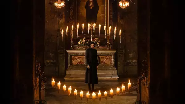 Foto de una monja vestida completamente de negro, rodeada de velas y detrás de ella una imagen de la virgen.