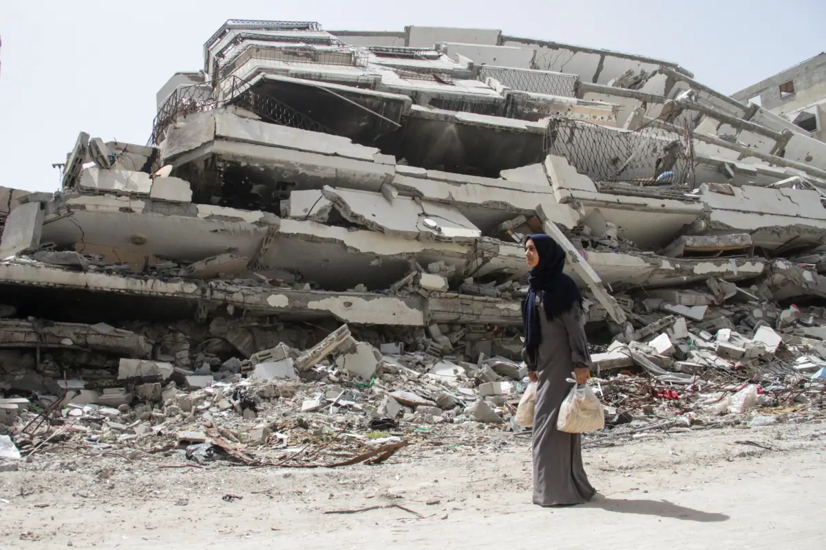 La mujer palestina Asmaa Al-Belbasi, regresando a su refugio después de comprar pan en la recientemente reabierta panadería Al-Sharq, pasa junto a las ruinas de una casa destruida durante la ofensiva militar de Israel, en medio del actual conflicto entre Israel y Hamas, en la ciudad de Gaza. 24 de abril de 2024.