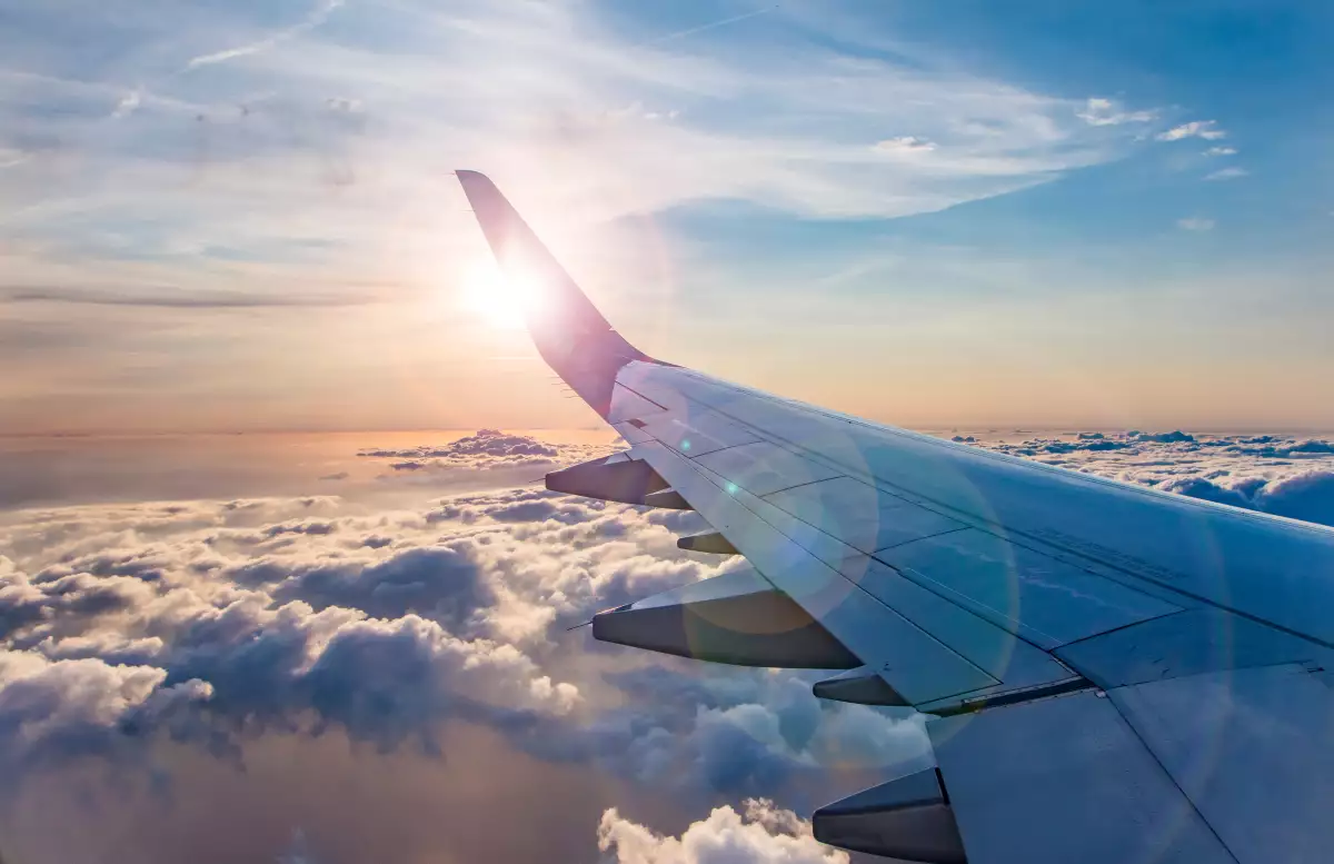 Ala de avión en un vuelo donde se observan nubes debajo y el sol al fondo.