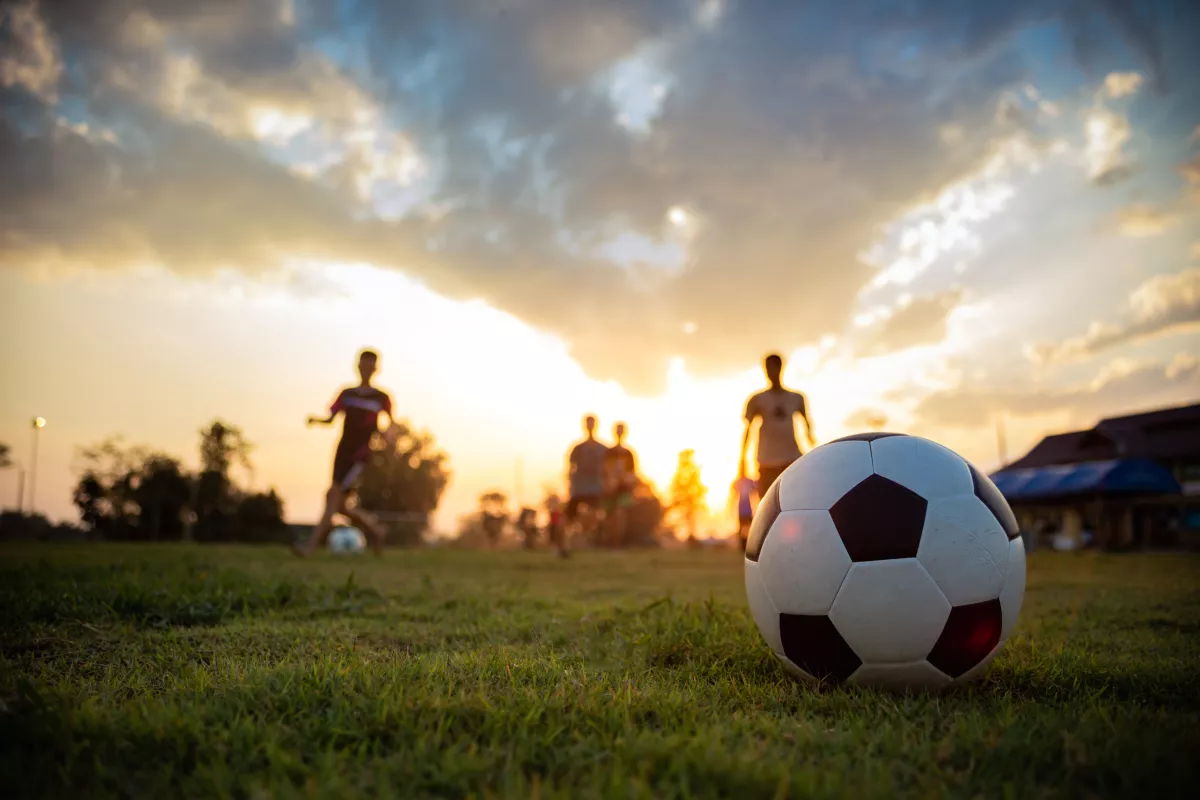 An action sport picture of a group of kids playing soccer football for exercise in community rural area under the sunset.