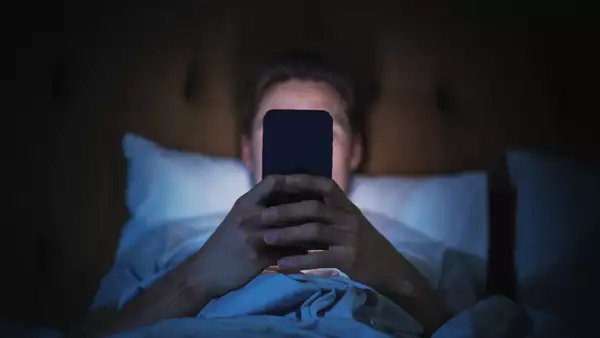 Foto de un hombre en una habitación a oscuras usando el celular con la pantalla brillante.
