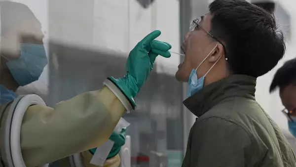 Un trabajador de la salud toma una muestra de un hisopo de un hombre para realizar la prueba del coronavirus Covid-19 en una estación de recolección de ácido nucleico en Beijing.