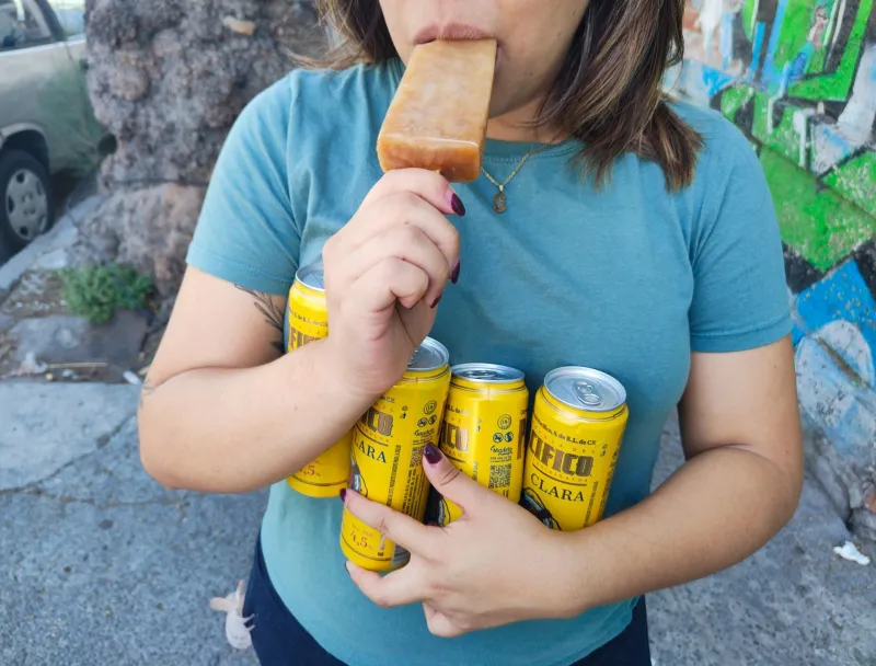 Una persona lleva consigo unas latas de cerveza mientras come una paleta de hielo.