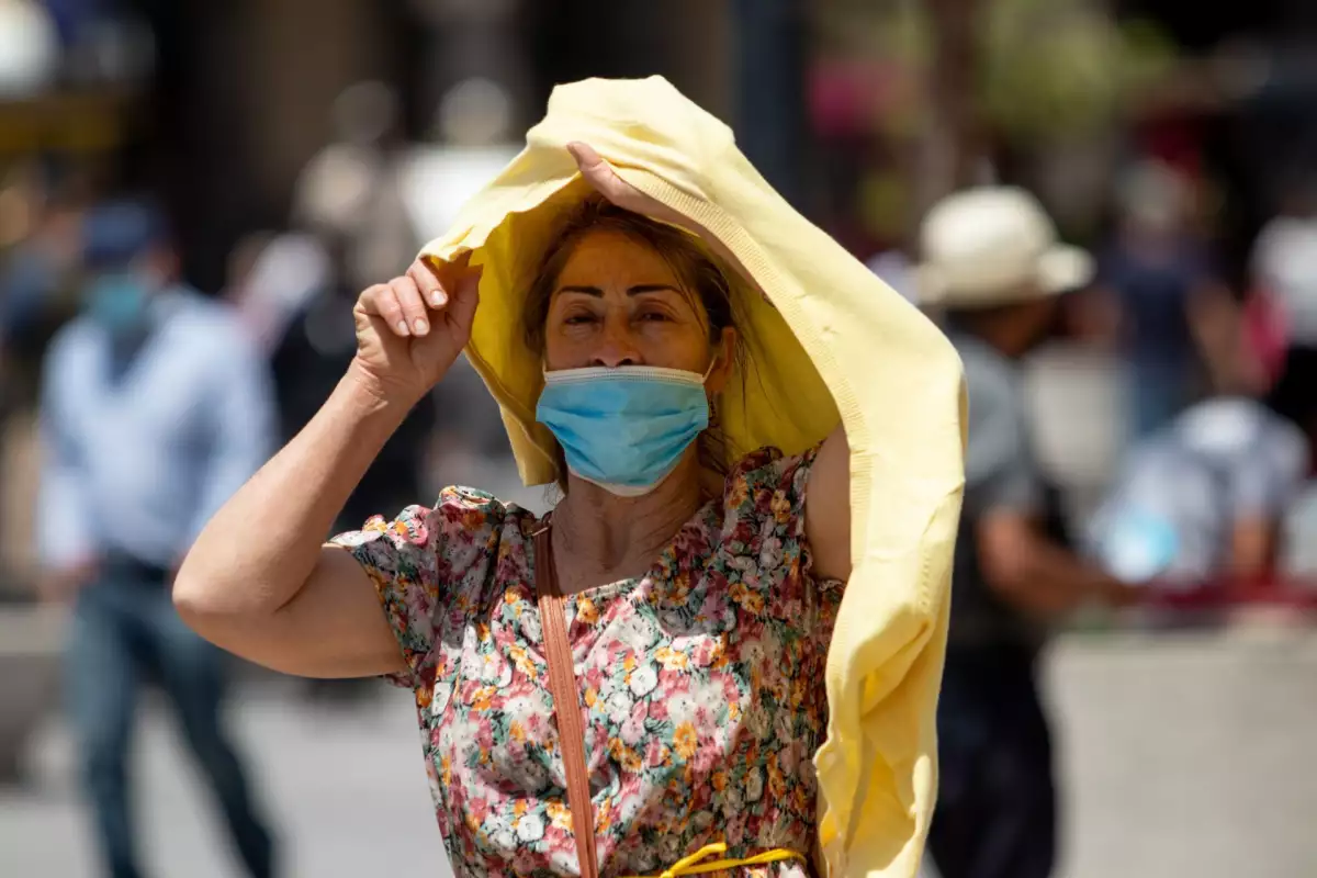 Se activa la alerta amarilla por calor en varias alcaldías, así está el pronóstico del clima en CDMX hoy. (mujer con cubrebocas cubriéndose del sol con una prenda).