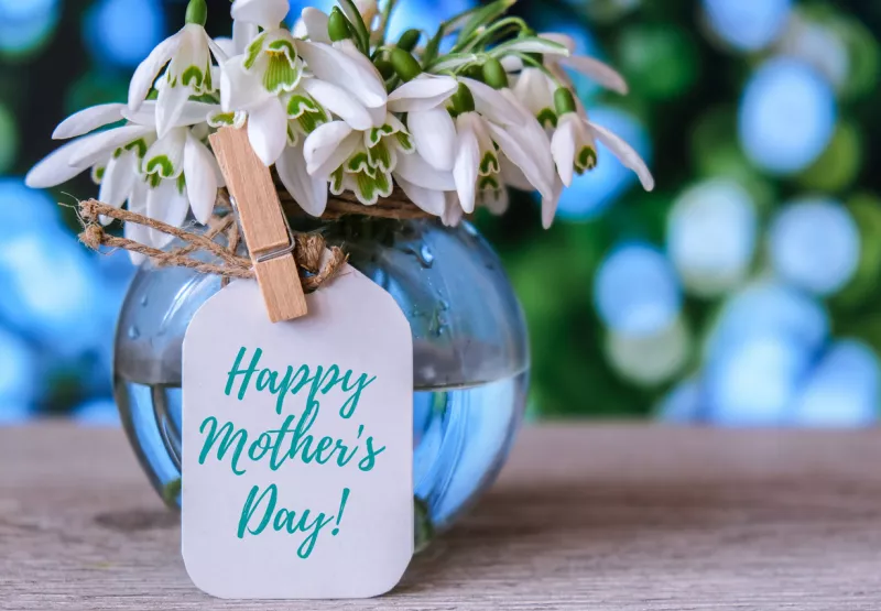 Letrero de Happy Mothers Day en un florero con flores blancas.