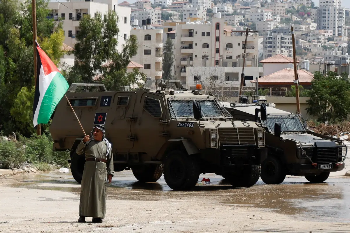 Un hombre sostiene la bandera palestina junto a vehículos militares israelíes durante la redada en Tulkarm, en Cisjordania ocupada por Israel, el 22 de agosto de 2024.