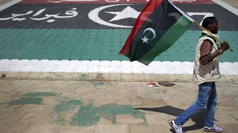 Hombre porta y camina frente a auna bandera de Libia en la ciudad de Benghazi