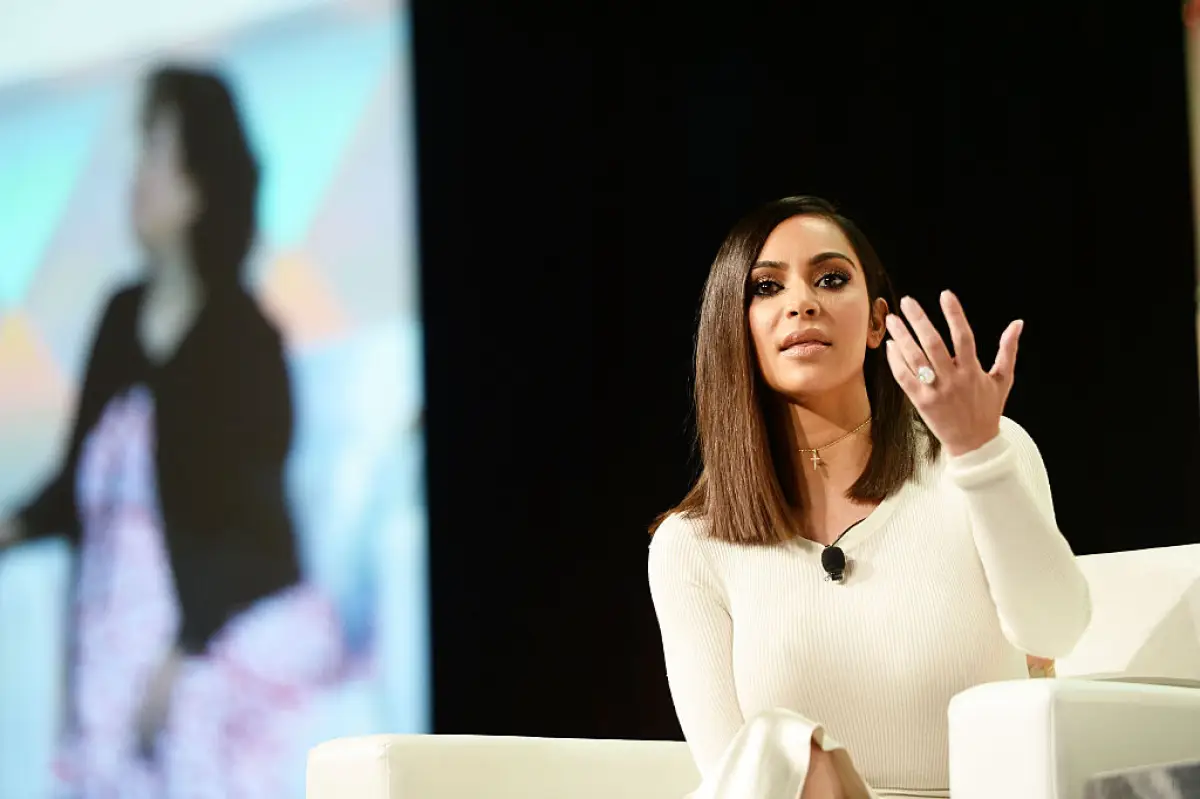 Foto de kim Kardashian en 2016 durante una rueda de prensa, va vestida de blanco y alza su mano izquierda frente a su cara mostrando su anillo de compromiso