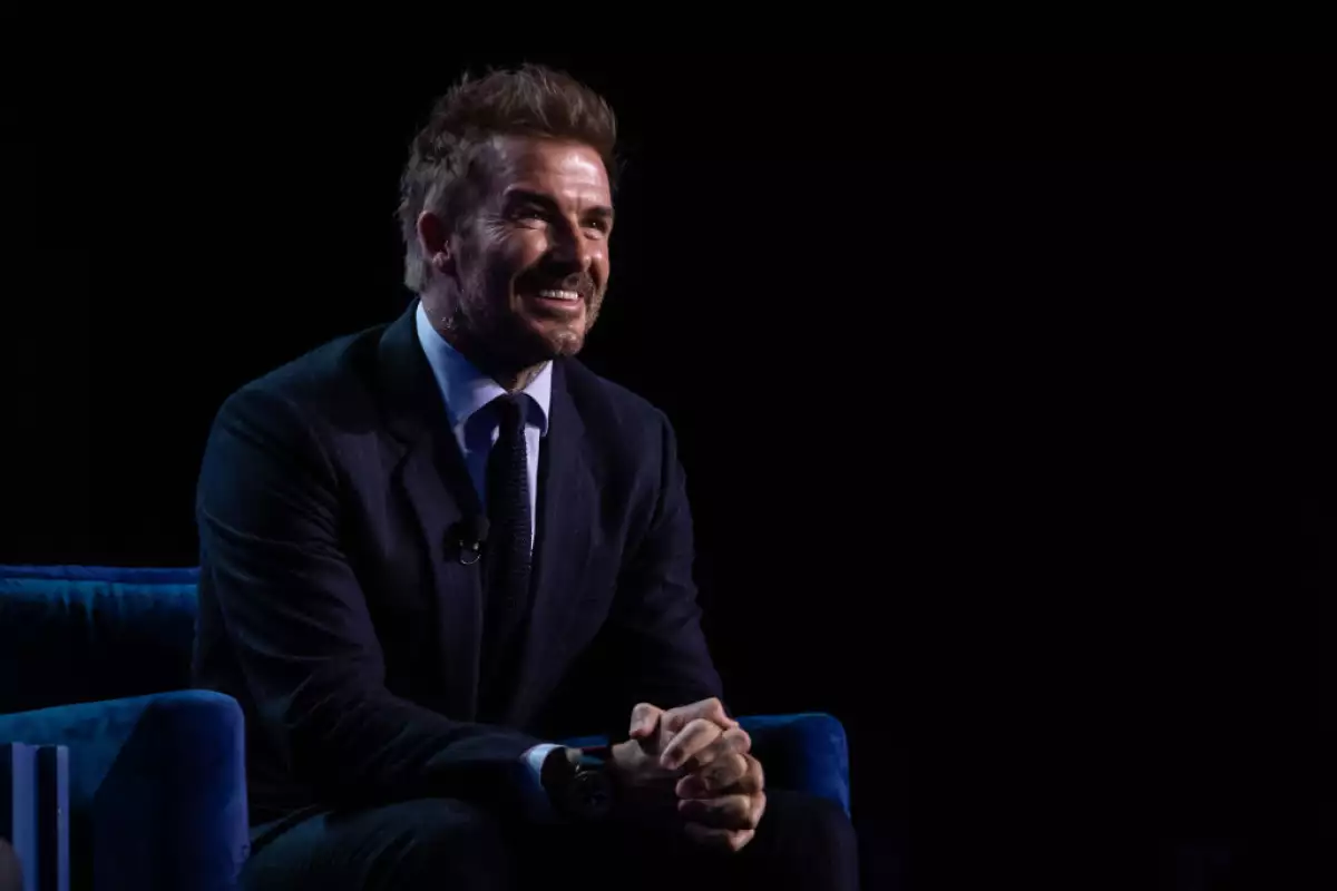 foto de david beckham sentado y sonriente con las manos entrelazadas al frente