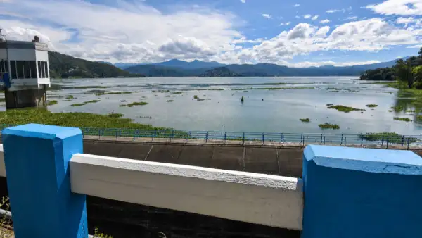 Un cuerpo de agua a cielo abierto; a las orillas hay árboles y una infraestructura en color blanco y azul.jpg