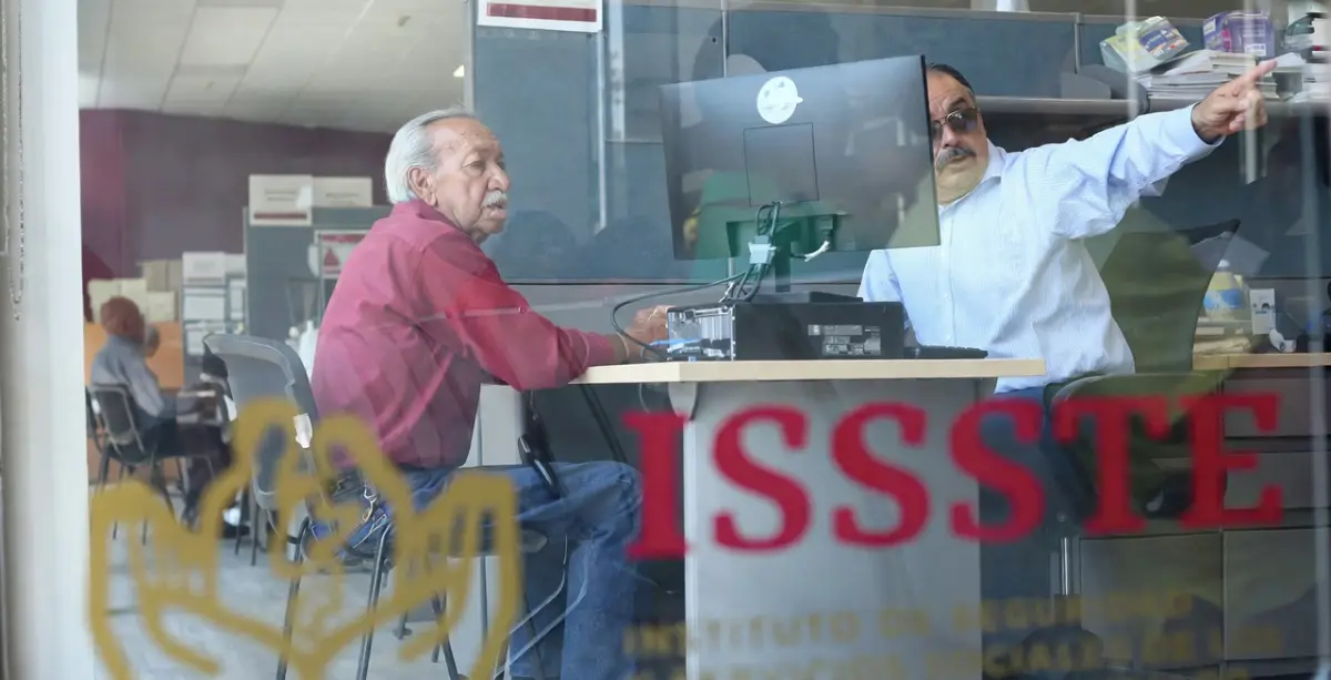 Adulto mayor frente a un trabajador del ISSSTE en las oficinas de la dependencia.