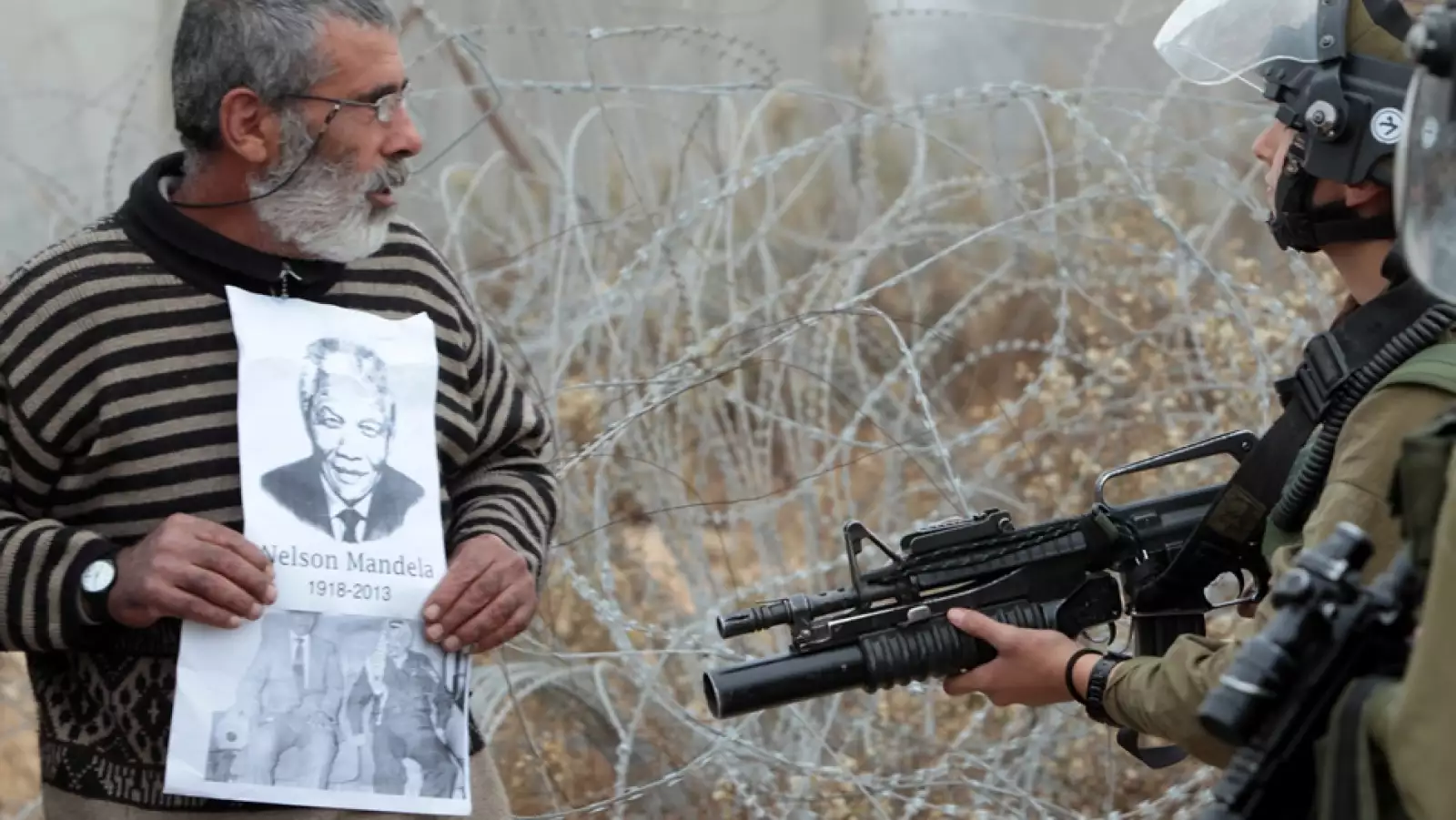 un palestino muestra una fotografia de nelson mandela a soldados israelies