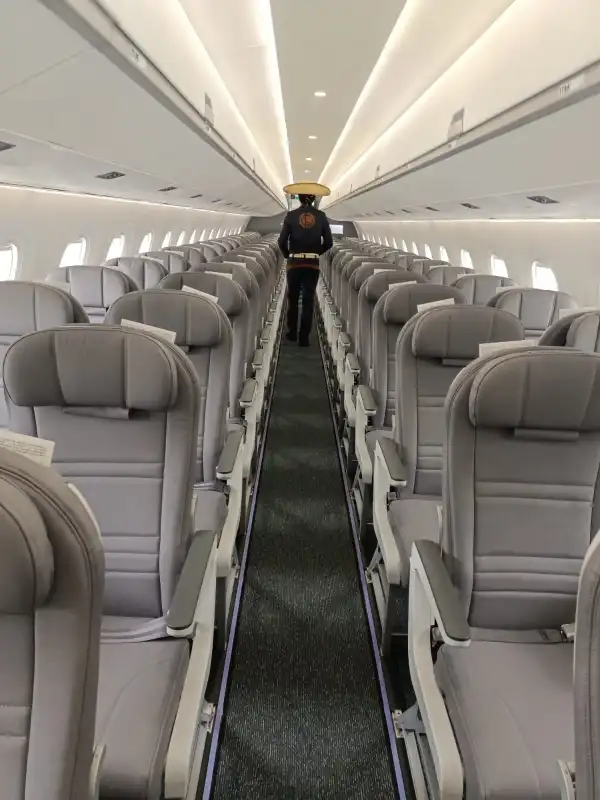 Interior de la aeronave con pasillo de suelo negro y asientos al lado de color gris, ventanas y parte superior de color blanco.jpeg