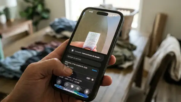 Imagen de un iPhone en primer plano mostrando en su pantalla la función de Búsqueda Visual. En el fondo se ve un entorno cotidiano en casa de alguien que está a punto de lavar su ropa.