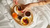 Desde arriba de una mujer sentada en la cama y esparciendo mermelada dulce sobre una tostada mientras desayunaba en el cuarto en la mañana soleada