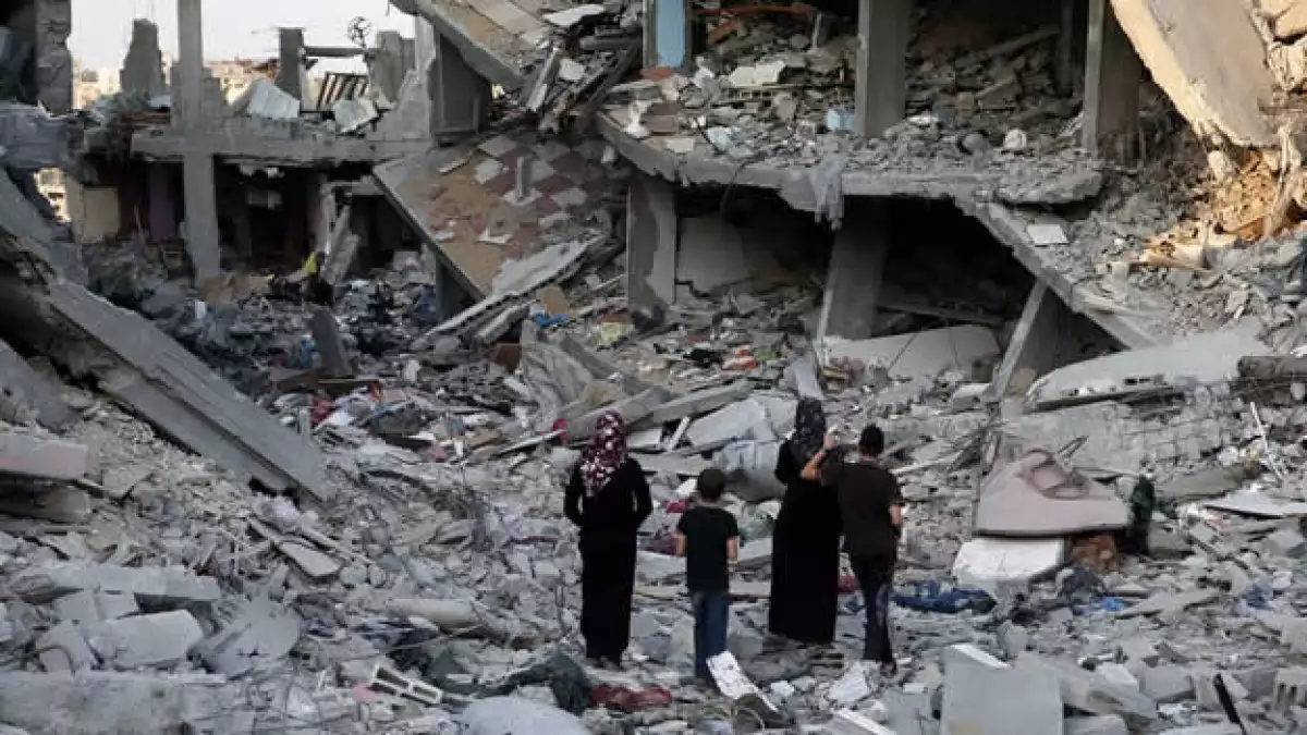 Un grupo de palestinos caminan entre los escombros de casas destruidas en Gaza este domingo