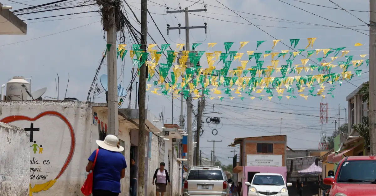 Una calle en donde se observan cables de luz, una camioneta, un coche blanco y uno rojo
