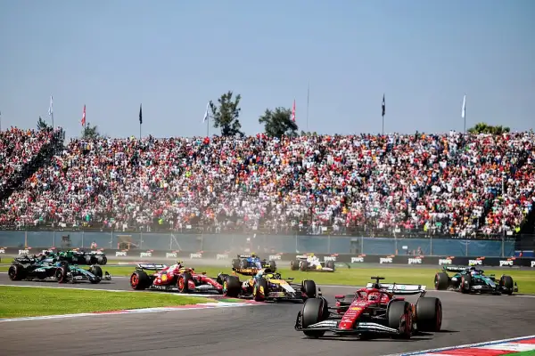 Monoplazas de Fórmula 1 compiten en el Autódromo Hermanos Rodríguez frente a unas gradas llenas de aficionados.