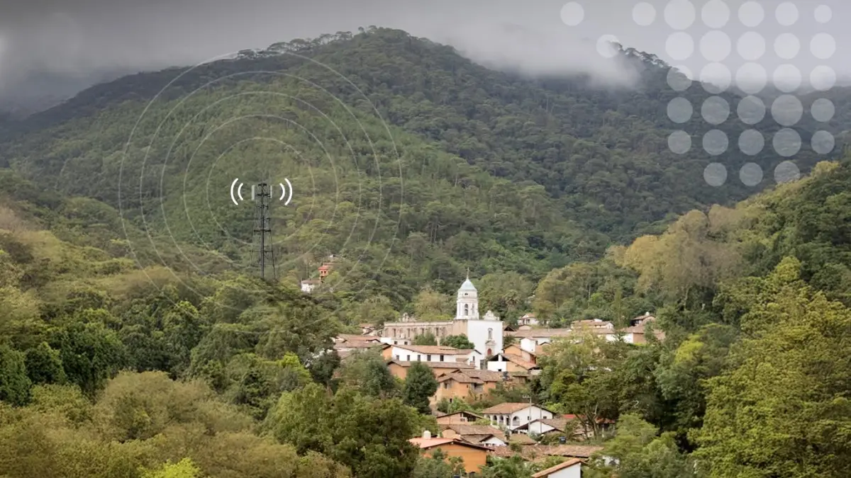 Un pueblito en medio de cerros con una antena de telecomunicaciones simulando dar señal de conectividad 