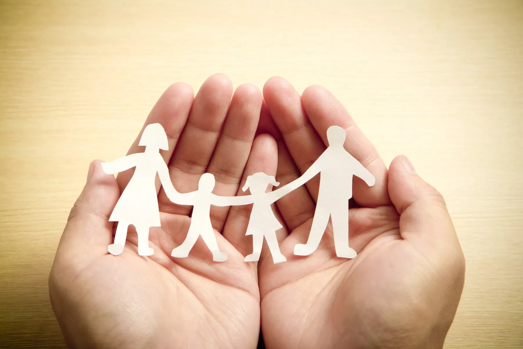 Paper family in hands with wooden texture background
