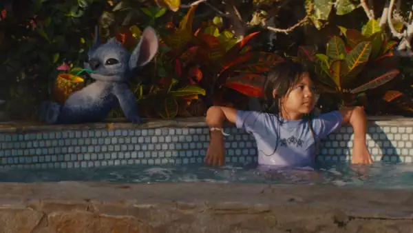 Foto de una escena de la película live action Lilo y Stitch, con Lilo en una alberca y Stitch sentado a su lado tomando una una bebida en una piña.