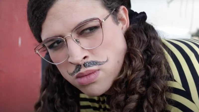 Foto de una escena del cortometraje Johanne Sacreblu, en el que se ve a la protagonista con lentes, bigote pintado y cabello rizado.
