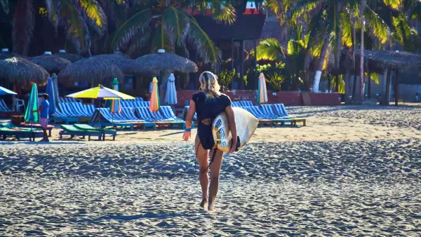girl walking with a surf board and lounges on the background, zicatela puerto escondido oaxaca