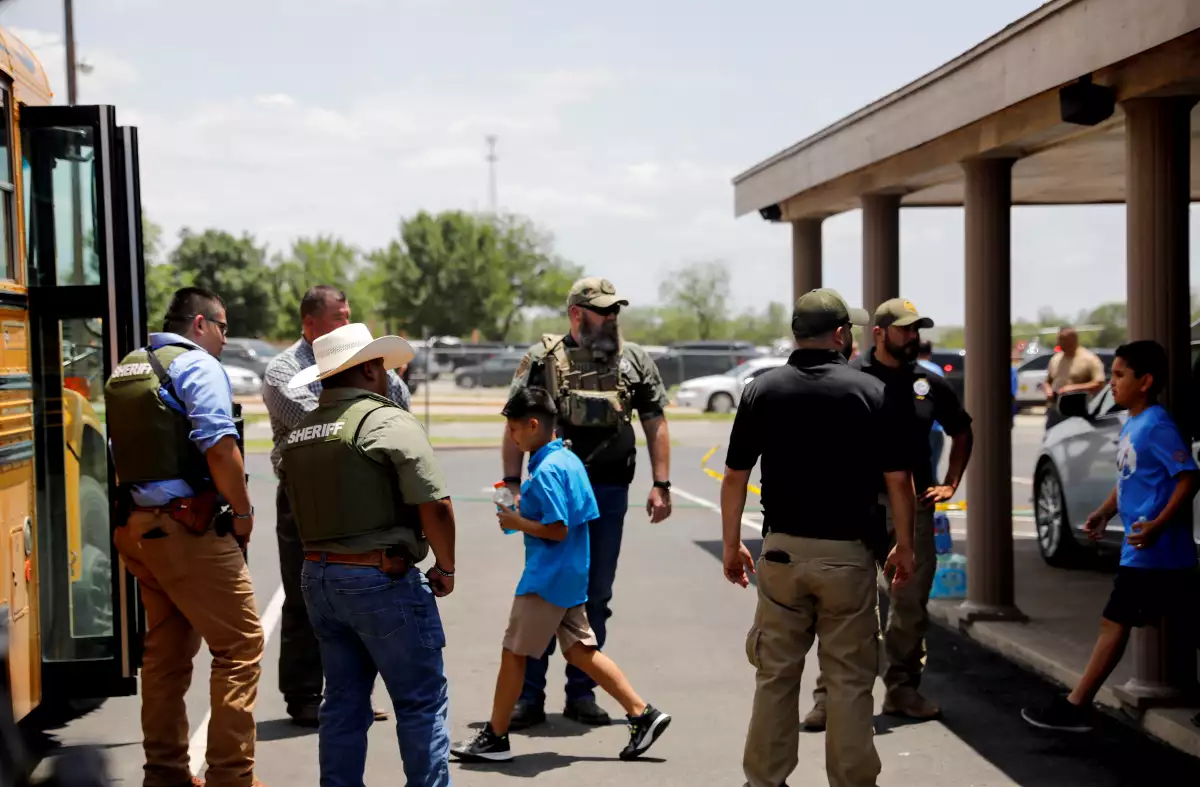 Niños vestidos con un uniforme azul y custodiados po policías entran en un autobús amarillo para evacuarlos de una escuela primaria de Uvalde, Texas, donde hubo un tiroteo. 