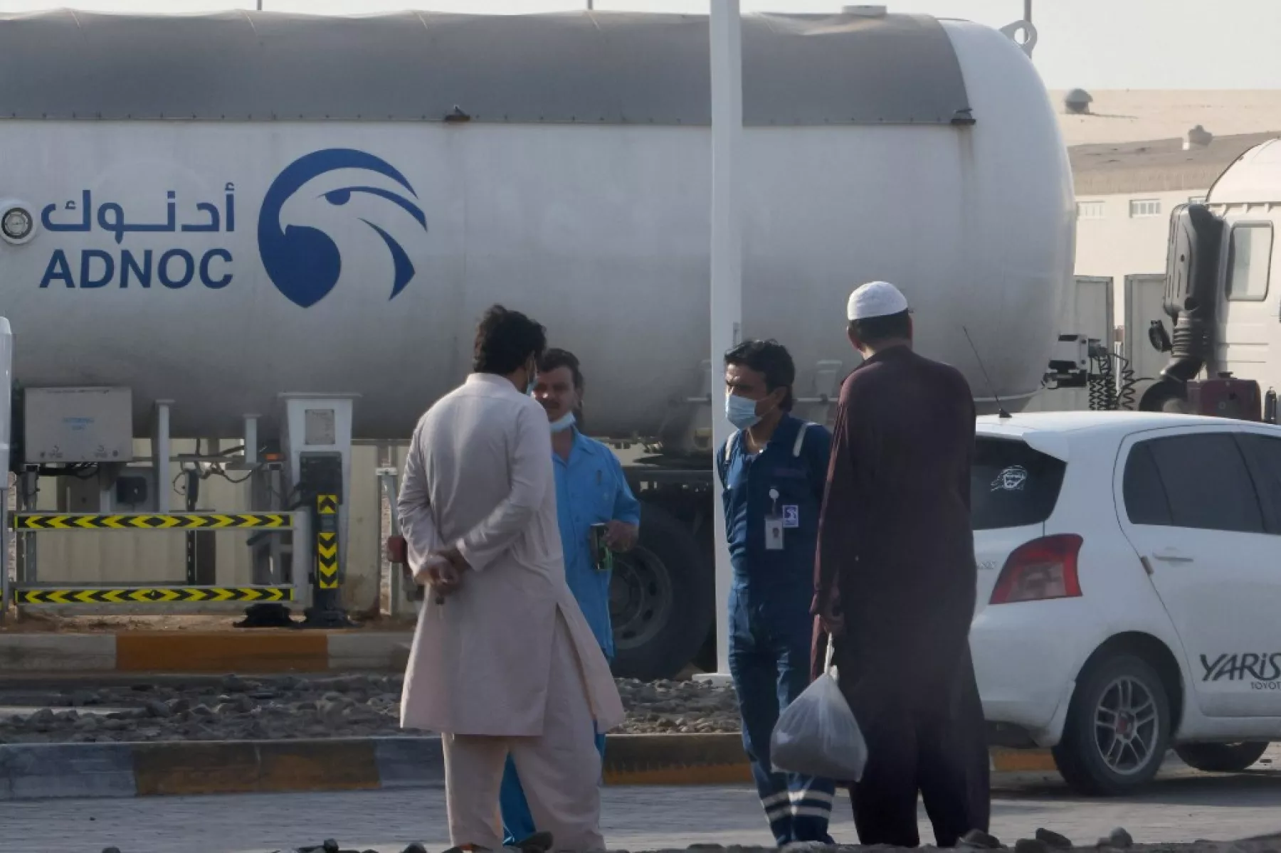 Hombres se paran junto a un tanque en una instalación de almacenamiento del gigante petrolero ADNOC en el distrito industrial de Msaffah. 